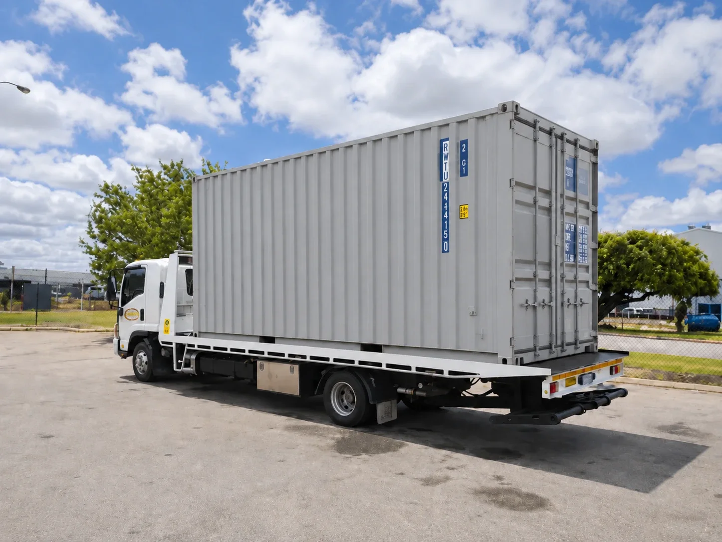 Shipping container loaded on a white tilt-tray truck in a car park