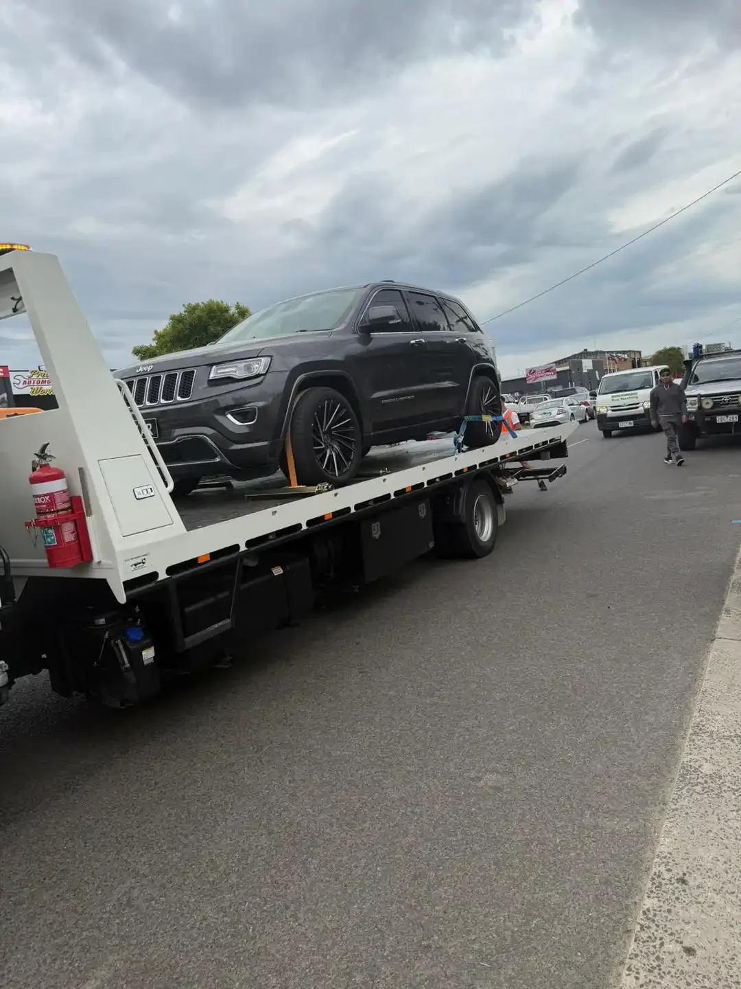 Dark grey Jeep Grand Cherokee strapped onto a tilt-tray truck