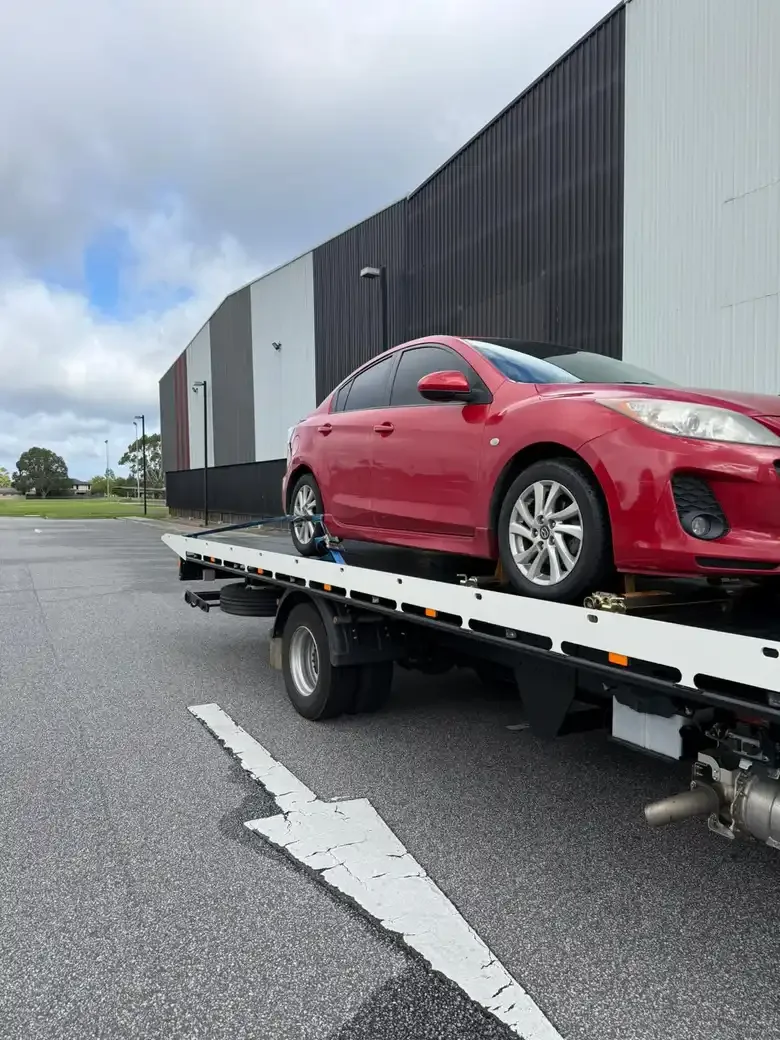 Red Mazda3 on a tilt-tray truck outside a warehouse