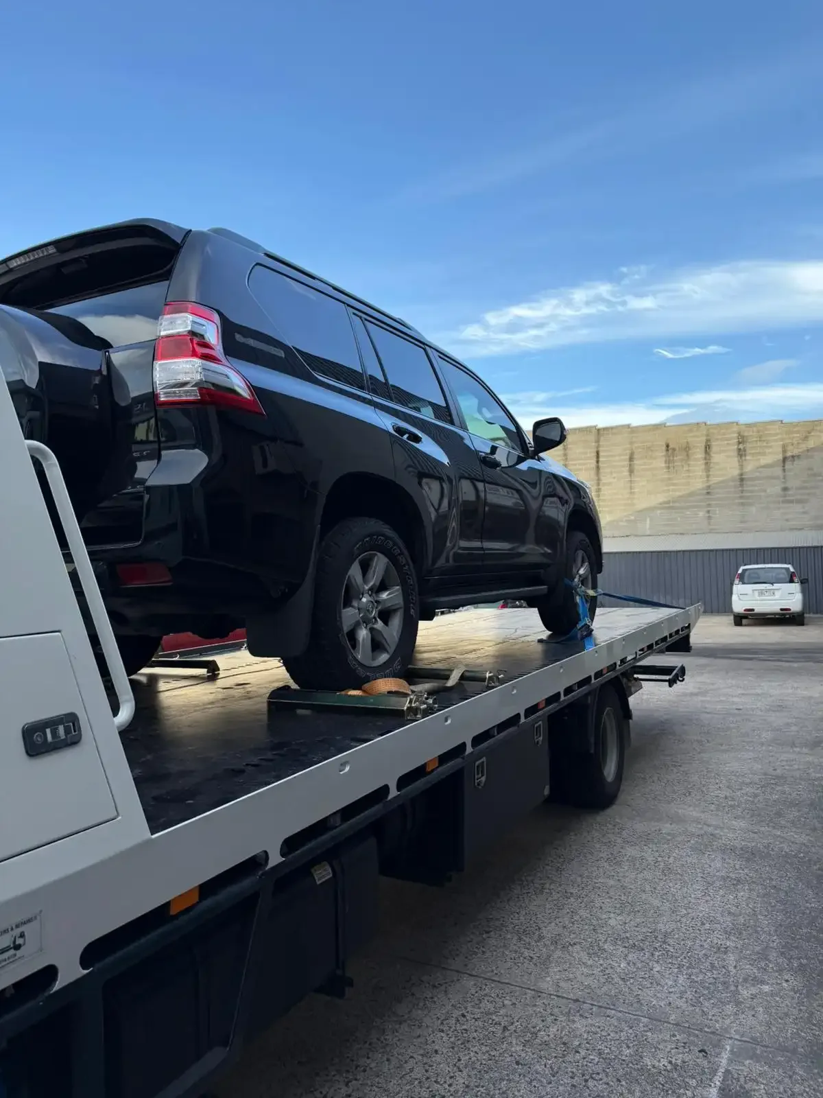 Black Toyota Prado strapped onto a tilt-tray truck