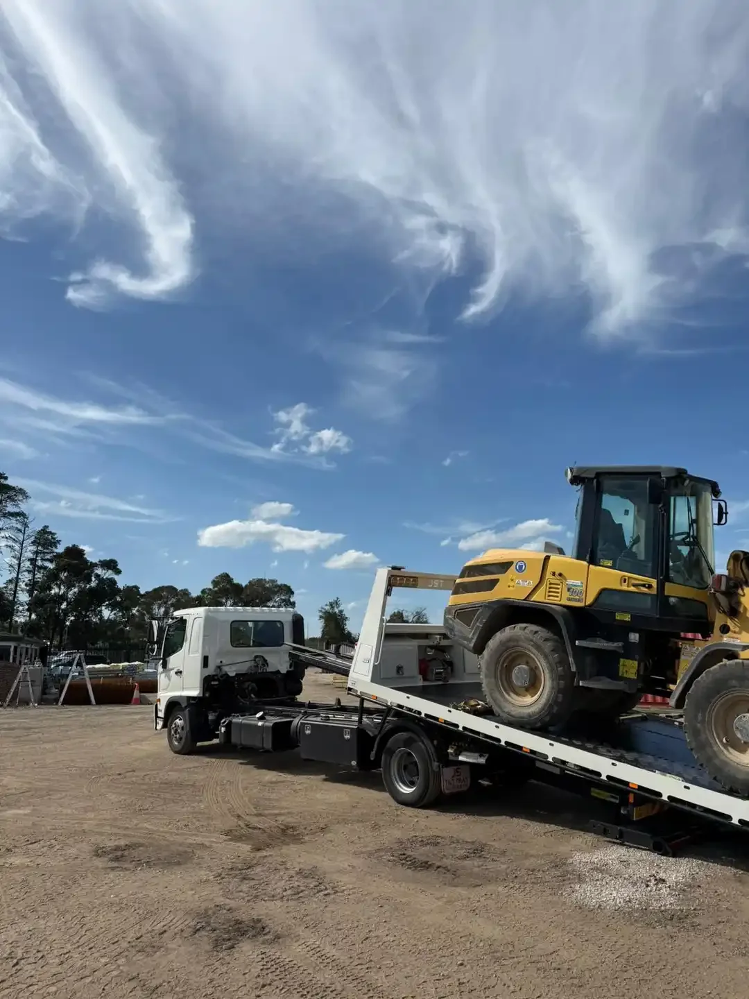 Yellow wheel loader on the tilted tray of a tow truck, on a dirt site